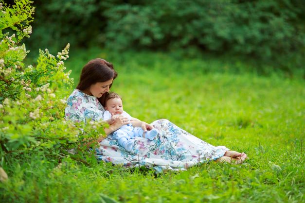 Baby and mama sitting outdoors in grass by flowering bush