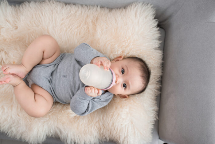 Baby drinking bottle on cream blanket in gray outfit
