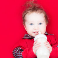 Baby Girl Drinking Warm Formula on Red Blanket