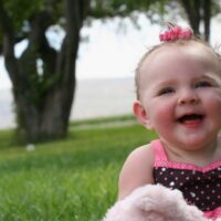 Baby girl in pink bow sitting in grass at park