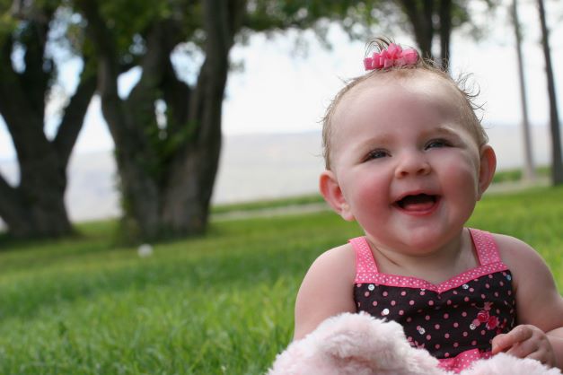 Baby girl in pink bow sitting in grass at park