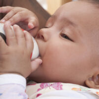 Parent feeding baby with closeup of baby holding bottle