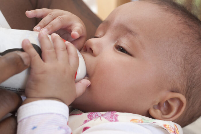 Parent feeding baby with closeup of baby holding bottle