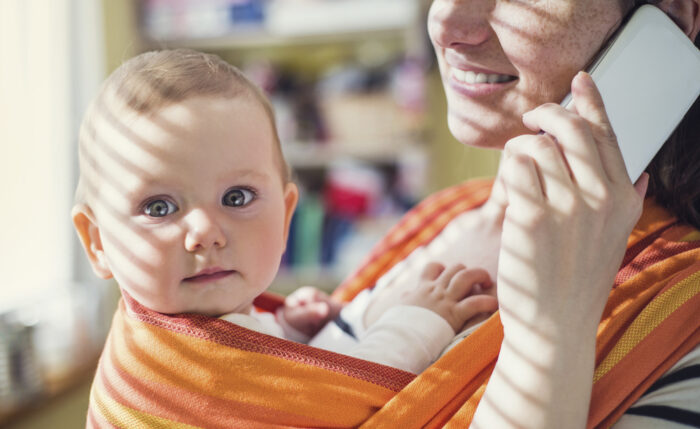 Close up of blue eyed baby with mom in sling baby carrier