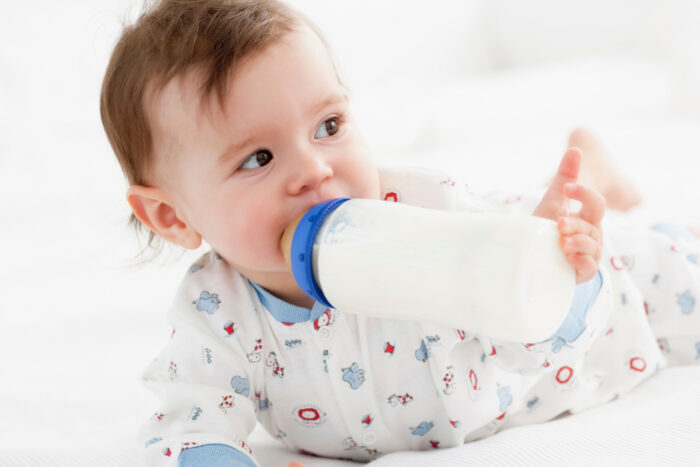 Cute baby sucking on bottle while on belly