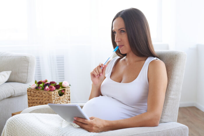 pregnant woman sitting with notebook thinking about baby names