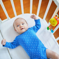 baby laying in crib with crib toy