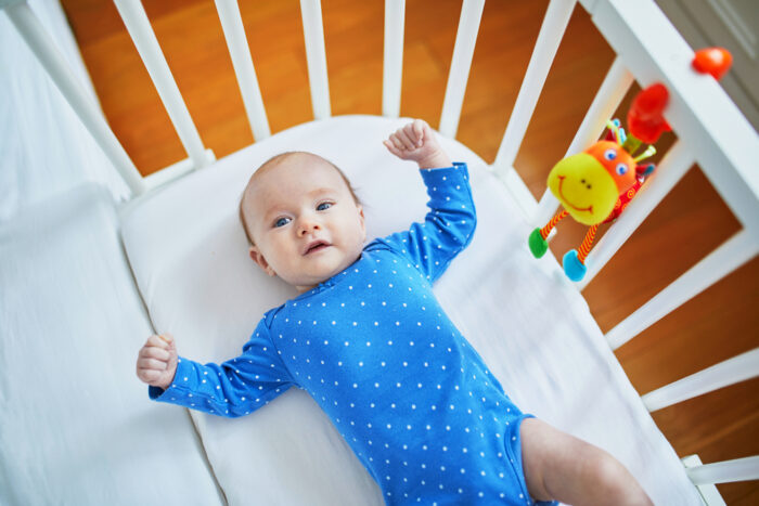 baby laying in crib with crib toy