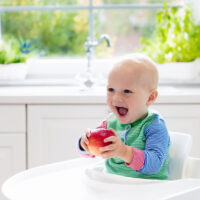 baby in a high chair with an apple