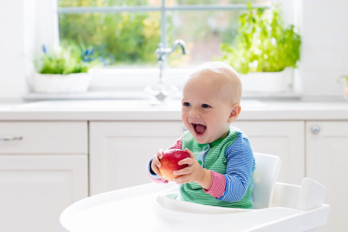 baby in a high chair with an apple