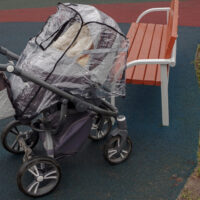 Empty stroller covered with stroller rain cover at playground on rainy day
