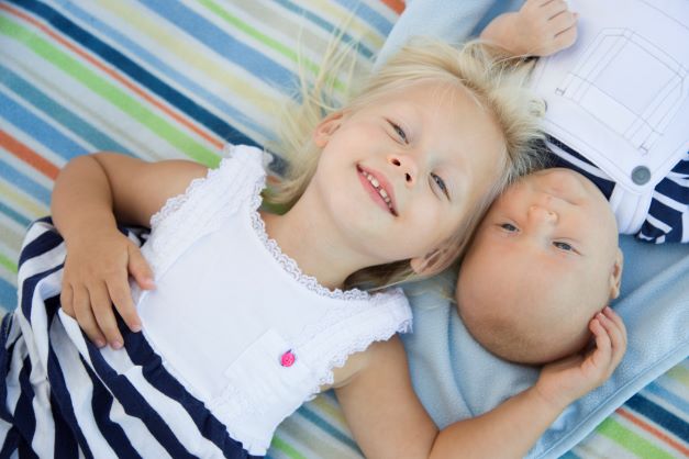 Happy big sister laying with baby brother on blanket