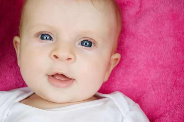 Blue eyed baby girl laying on pink blanket