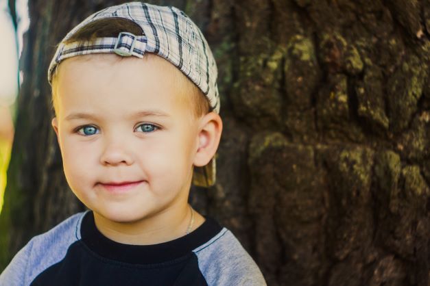 Blue eyed young boy with plaid hat on backwards