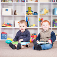 Two toddlers reading in front of toy and book shelves