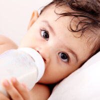 Brown haired baby drinking formula from bottle