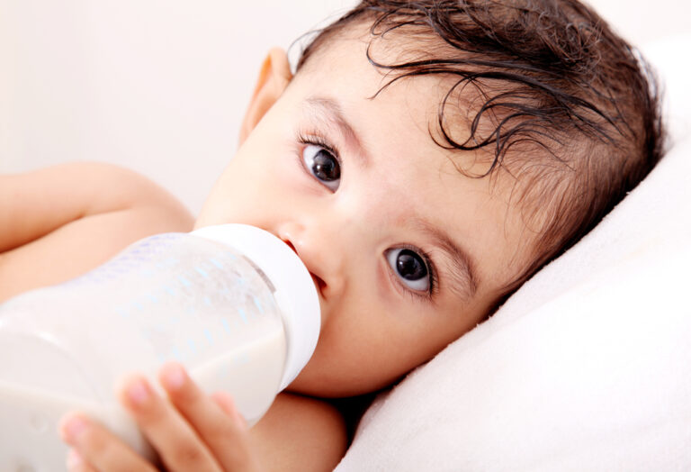 Brown haired baby drinking formula from bottle