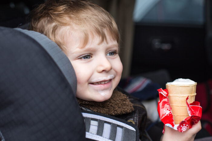 Child eating ice cream and smiling in his car seat