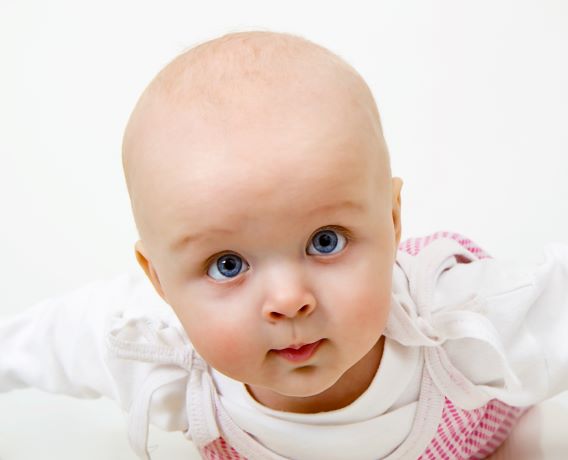 Close up of blue eyed infant girl on belly