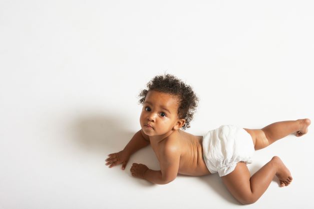 Curly haired baby boy in diaper crawling on white floor