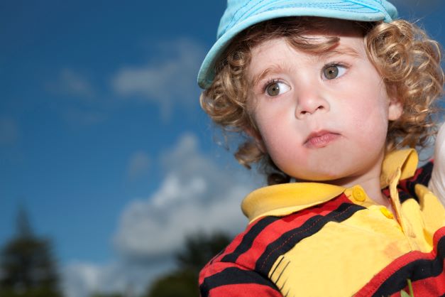 Curly haired toddler boy wearing a blue cap and striped shirt