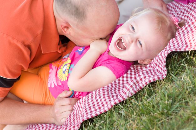 Dad tickling baby girl on blanket at the park