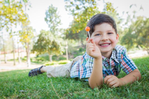 Dark haired boy laying outside enjoying his lollipop