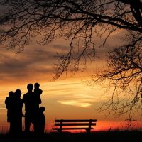 Family with sunset and park bench behind them