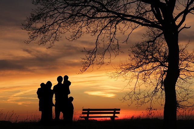 Family with sunset and park bench behind them