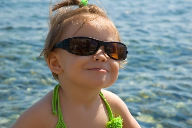 Happy toddler girl in sunglasses at the beach