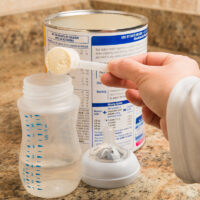 mother scooping baby formula into a baby bottle