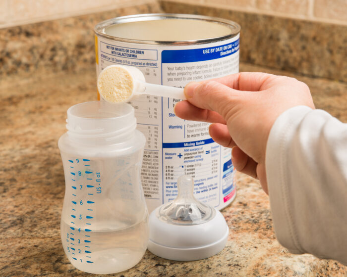 mother scooping baby formula into a baby bottle