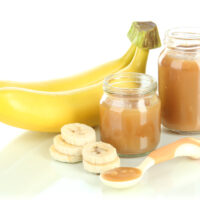 Baby food puree in jars with bananas isolated on white