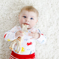 baby laying on the ground chewing on a teether