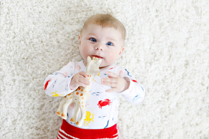 baby laying on the ground chewing on a teether