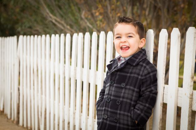 Little boy in plaid coat standing by white fence