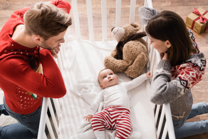 High view of mom and dad peering in crib at baby