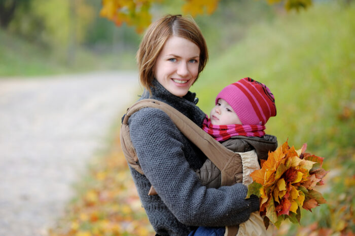 Mom with baby in carrier with fall leaves in her hand