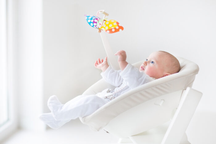 baby sitting in a rocker playing with mobile