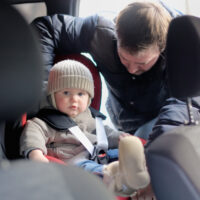 Parent strapping toddler boy in car seat