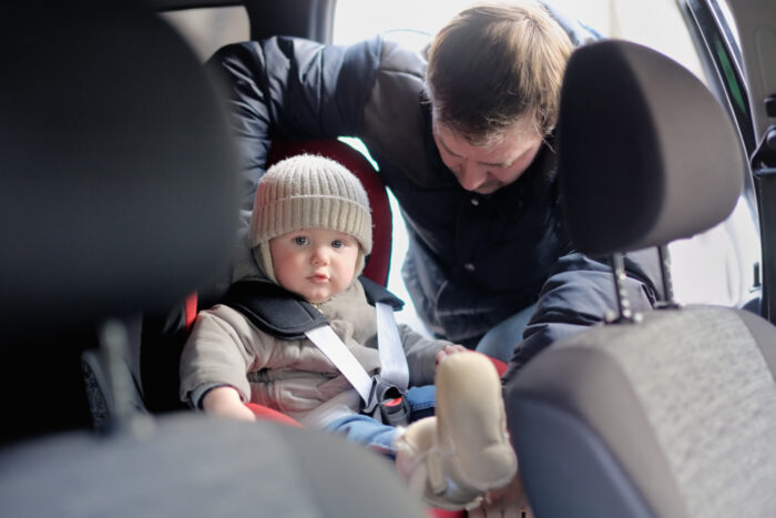 Parent strapping toddler boy in car seat