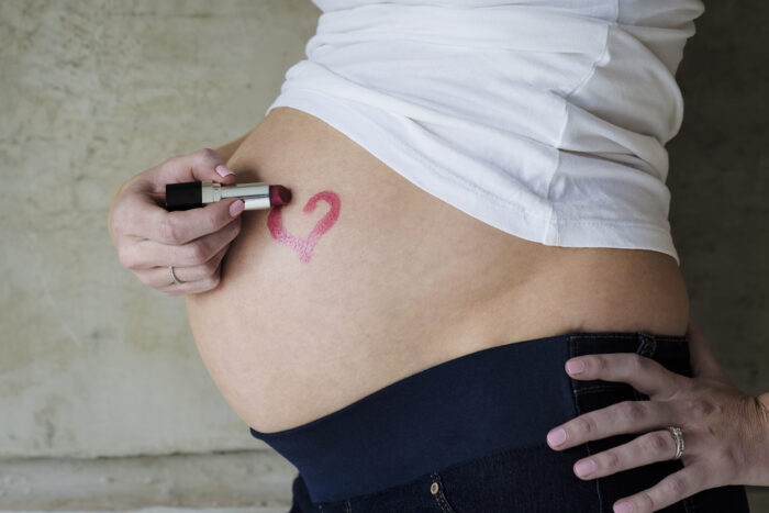 Pregnant woman with lipstick heart on baby bump