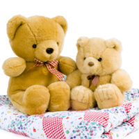 two teddy bears sitting on a baby quilt