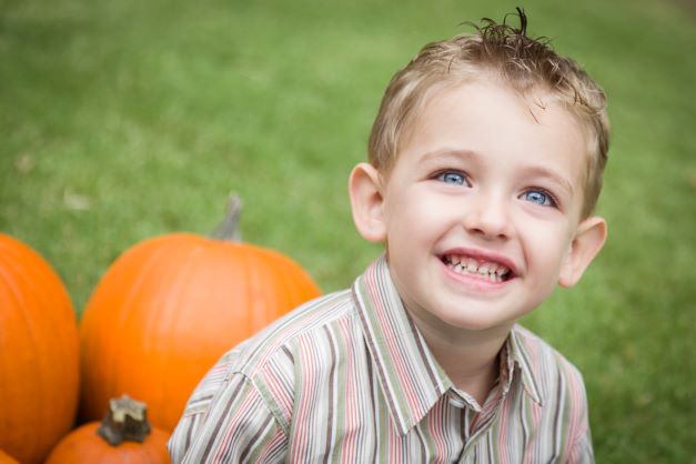Smiling school aged boy sitting with pumpkins