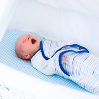 Little swaddled baby in white bed