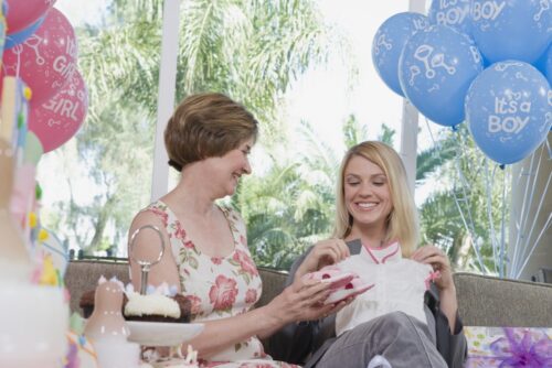 Mother showing baby clothes to pregnant woman at a baby shower