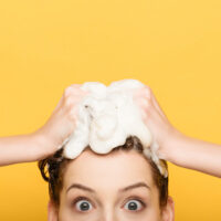 Pregnant woman shampooing hair on yellow background