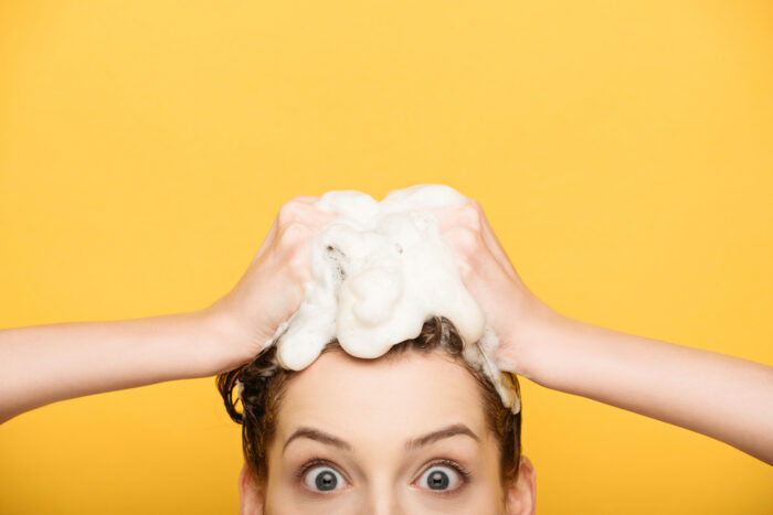 Pregnant woman shampooing hair on yellow background